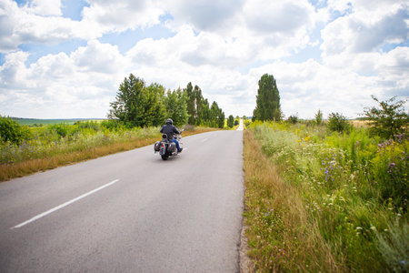 A biker on a motorcycle rides along the road between rural fields. Summer, sunny day, beautiful skyの写真素材