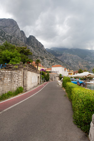 A picturesque coastal town nestled against dramatic mountains under a cloudy sky, features a paved road with a bike lane.の写真素材