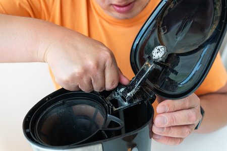 A person cleans a dirty coffee maker, removing coffee grounds and residue from the filter and housing.の写真素材