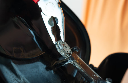 A close-up shot shows a person using pliers to carefully remove a small, dusty part from a broken...