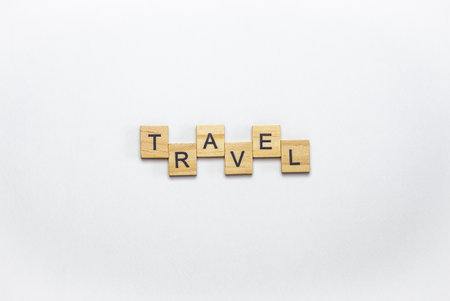 Wooden letter tiles spell out the word 'TRAVEL' on a white background, ideal for travel-themed...