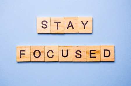 Wooden blocks spelling out the motivational message 'Stay Focused' on a light blue background.の写真素材