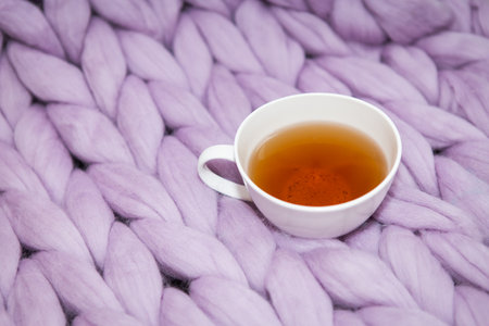 The concept of coziness and comfort is a pink-lavender knitted blanket with a white cup of hot tea...
