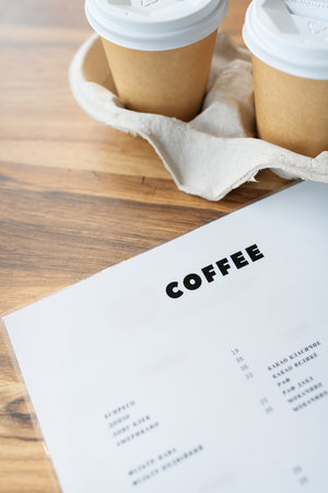 A cafe menu and two takeaway coffee cups rest on a wooden table, showcasing a simple yet stylish coffee shop setting.の写真素材