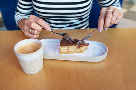 A woman enjoys a delicious slice of chocolate cake with coffee at a cafe.の写真素材