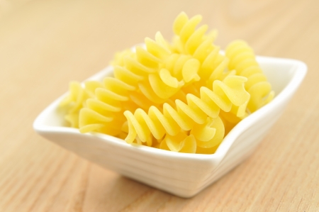 Uncooked fusilli in a small bowl, italian pasta, wooden background, selective focusの写真素材