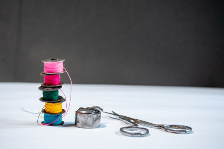 Various colored threads are wound on bobbins of a sewing machine and a scissor, placed against a white background with ample copy spaceの写真素材