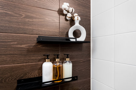 Accessories on black shelves: a vase with cotton, bottles with dispensers, background â brown tile with wood texture and white tile.の写真素材
