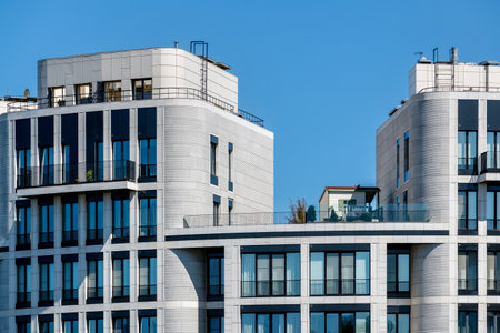 Facades of modern residential buildings with light cladding, panoramic windows, and balconies against a clear blue sky.の写真素材