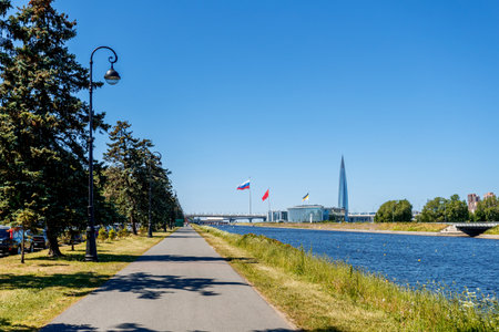 Lakhta Center and a complex of buildings with flags are visible across the river, a lamppost on the left, the foreground is framed by branches.の写真素材