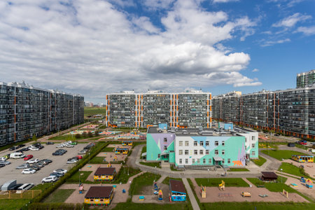 Modern residential complex with multi-story buildings, parking, and a bright kindergarten building with playgrounds.の写真素材