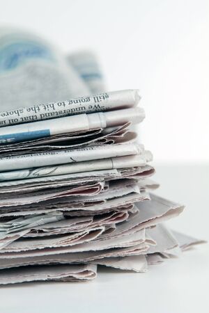 Stack of newspapers sit on a white background in vertical format.