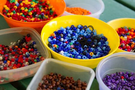 Bright and colorful hair beads for braiding, arranged and grouped by shades and color, sit in separate bowls on a table.の写真素材