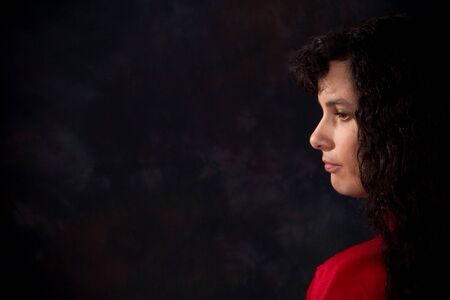 Serious and somber looking woman against a dark background. Copy space on left.の写真素材