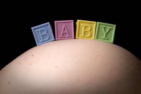 Four colorful lettered baby blocks spell out the word BABY as they sit on a pregnant woman's swollen abdomen.の写真素材