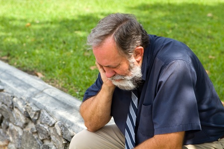 Businessman depressed by economic conditions sits melancholic in a park with his head in his hand.の写真素材
