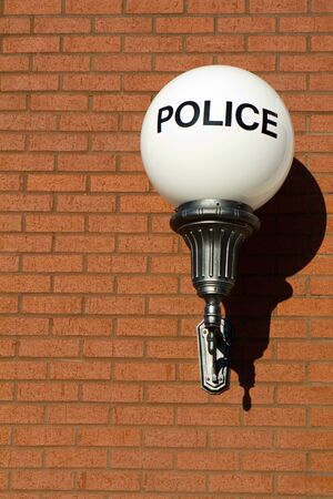 Old fashioned vintage police sign on a globe light hangs on a brick wall outside a retro designed city police station の写真素材