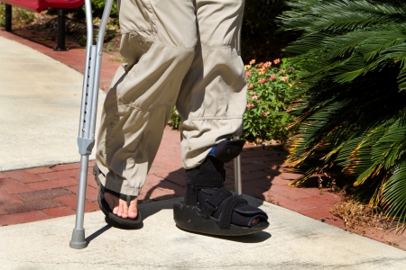 Man uses crutches along with a foot and ankle brace to help him walk after an accidental injury の写真素材