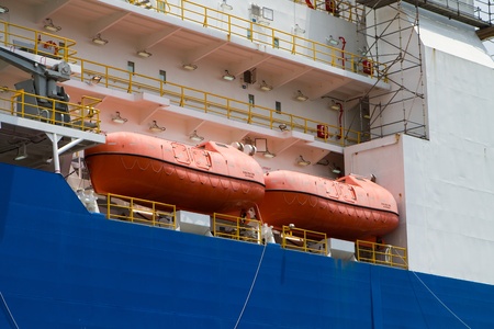Orange survival lifeboats sit on the deck of an industrial ship の写真素材