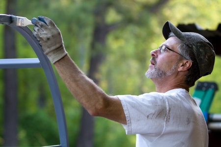 Mature man paints ironwork with paintbrush applying primer to the metal.の写真素材