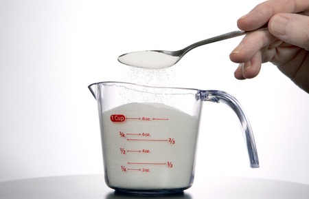 Man pours a spoonful of sugar into a measuring cup.の写真素材
