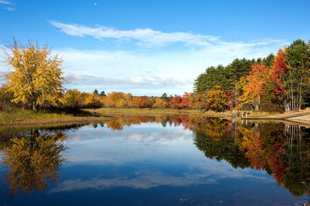 Vibrant autumn leaves and colors of fall tree foliage reflect on the waters of Lake Sabago, Maine in...