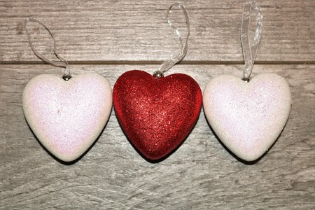 Two white and one red glitter hearts on a wood grain background. Room for text on hearts.の写真素材