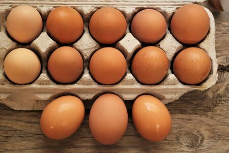 Top view of farm fresh brown eggs in a carton, on a wood table.