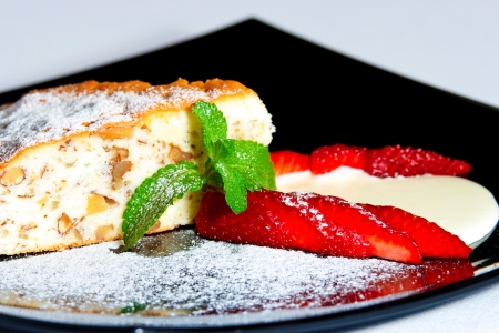 Cake with fresh strawberries, mint and cream on a dark plateの写真素材