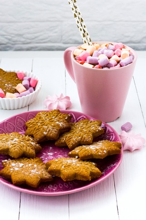 Christmas cocoa with marshmallow in a pink cup and ginger biscuit on a wooden tableの写真素材