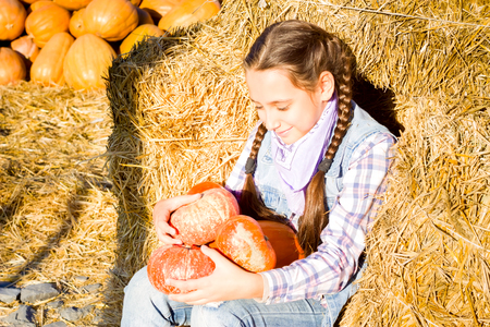 Young teenager girl sitting on straw with pumkins on farm market. Family celebrating thanksgiving or halloween.の写真素材