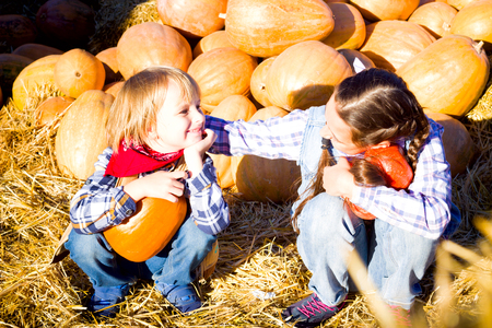 Cute Young Brother and Sister Children sitting on straw with pumkins on farm market. Family celebrating thanksgiving or halloween.の写真素材