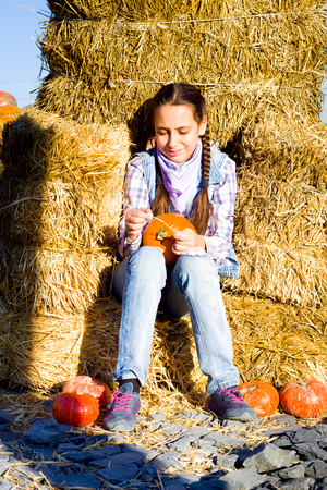 Young teenager girl sitting on straw with pumkins on farm market. Family celebrating thanksgiving or halloween.の写真素材