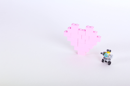The bricks of the plastic constructor in the form of pink heart whith little robot. White backgroundの写真素材
