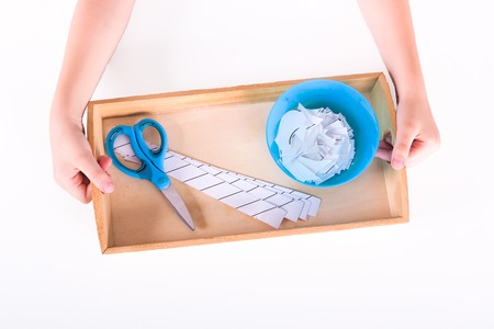 Children's hands hold a wooden tray with montessori materials for a lesson from the practical life...