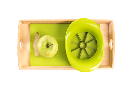 A wooden tray with montessori materials for a lesson from the practical life zone. Apple slicer, cutting board,green apple. Isolate on white background. Flat layの写真素材