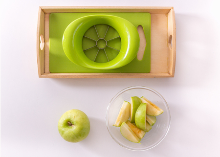 A wooden tray with montessori materials for a lesson from the practical life zone. Apple slicer, cutting board,green apple. Isolate on white background. Flat layの写真素材