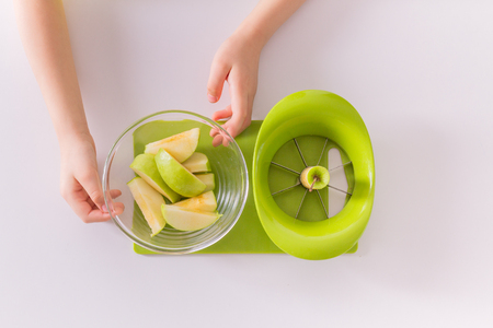Children's hands are putting sliced apple into a bowl. Flat lay. Montessori materials for a lesson from the practical lifeの写真素材