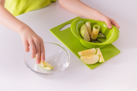 Children's hands are putting sliced apple into a bowlの写真素材