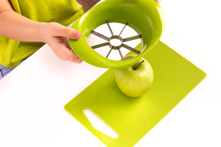 Children's hands holding an apple slicer and cutting green apple. Montessori materials for a lesson from the practical life zone.の写真素材