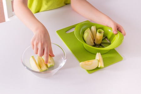 Children's hands are putting sliced apple into a bowl. Montessori materials for a lesson from the practical lifeの写真素材