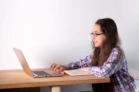 Distance learning at home. Teen girl with laptop does homework, reads a book, search information on the Internet. Elearning concept.の写真素材