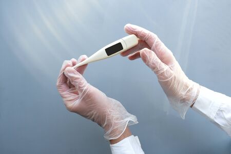 Womens hands in medical gloves hold a thermometer. Blue background. Healthcare medical doctor...