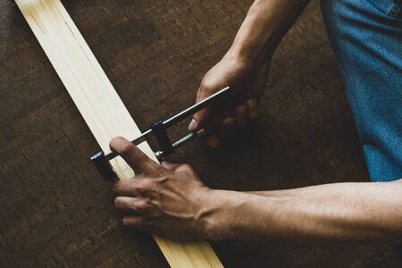 Mens hands fasten the clamp to the wooden rails, making a measurement before cutting. Repair concept