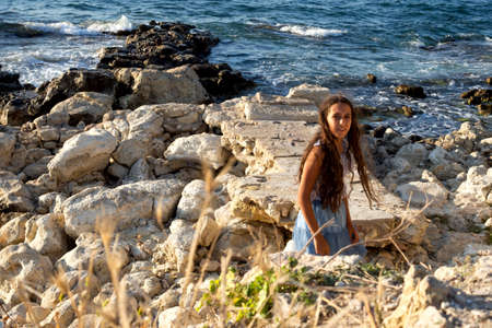 Young beautiful caucasian cute girl outdoor on the seashore on the sand among large beautiful yellow stonesの写真素材