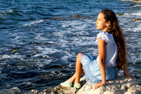 Young beautiful caucasian cute girl outdoor on the seashore on the sand among large beautiful yellow stonesの写真素材
