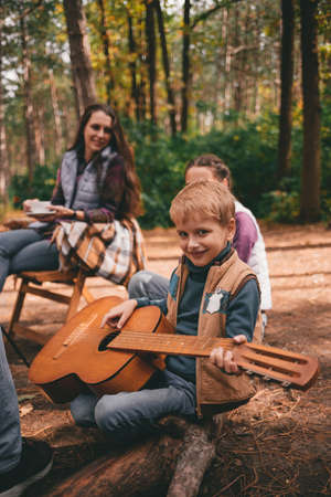 Happy family on a camping trip relaxing in the autumn forest. A boy holds a guitar in his handsの写真素材