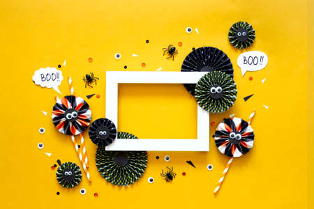 Happy halloween holiday concept. DIY paper decorations on bright yellow background with black spider, eyes, confetti. Halloween party greeting card. Spelling word Boo. Frame mock up with copy spaceの写真素材