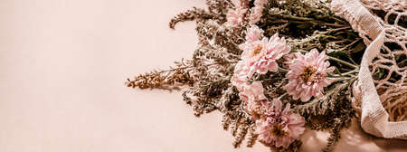 Beautiful bouquet of pink chrysanthemum flowers in a mesh bag on pale pink beige background. Trending minimalist horizontal banner with copy space for text.の写真素材