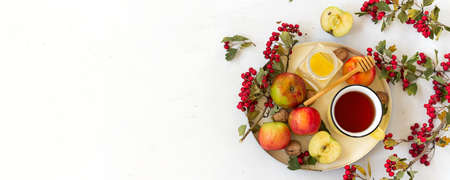 Wide banner with copy space for text. Cozy autumn hot spiced tea with honey, apples and red hawthorn berries on a tray. Still life on white background. Flat layの写真素材